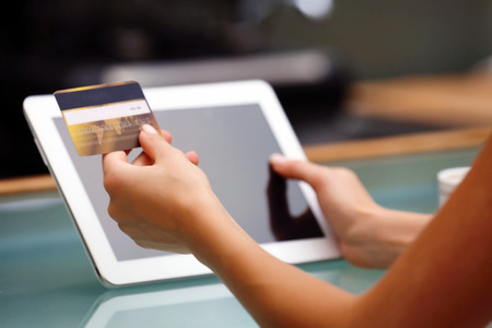 Female hands holding credit card with digital tablet on table close upの写真素材