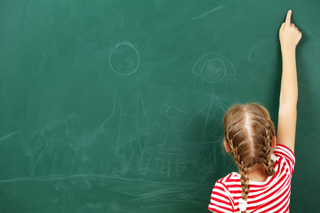 Little girl pointing at something at black chalkboard in classroomの写真素材