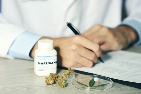 Doctor writing on prescription blank and bottle with medical cannabis on table close upの写真素材