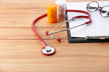 Medical stethoscope with clipboard and pills on wooden table close upの写真素材