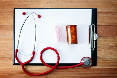 Medical stethoscope with clipboard and pills on wooden table close upの写真素材