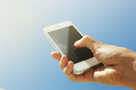 Female hand holding smart mobile phone on blue sky backgroundの写真素材