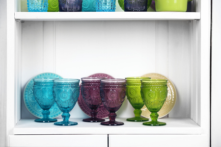 Clean glasses, plates and cutlery on shelf in kitchen cupboardの写真素材