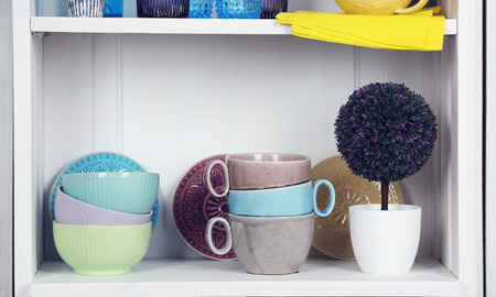 Clean glasses, plates and cutlery on shelf in kitchen cupboardの写真素材