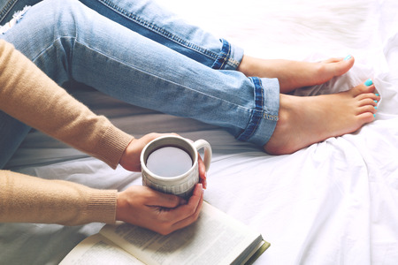 Woman on the bed with old book and cup of coffee, top view pointの写真素材