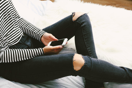 Woman in black jeans watching phone on bed top view pointの写真素材