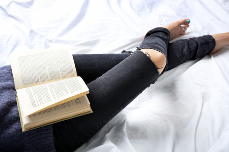 Woman in black jeans reading book on bed top view point