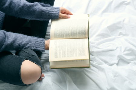 Woman in black jeans reading book on bed top view pointの写真素材