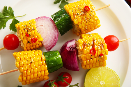 Delicious grilled corn and vegetables on white plateの写真素材