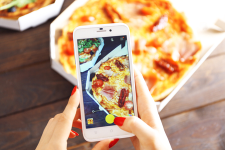 Woman taking a photo of pizza with the smartphoneの写真素材