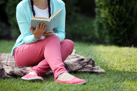 Young woman with book sitting on green grass outdoorsの写真素材