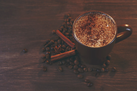 Tasty hot coffee with roasted beans and cinnamon around on wooden background