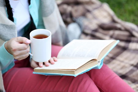 Young woman with book sitting on green grass outdoorsの写真素材