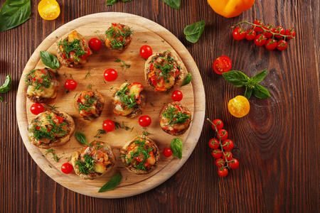 A wooden tablet with stuffed mushrooms and vegetables on the table, top viewの写真素材