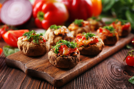 A wooden tablet with stuffed mushrooms and vegetables on the tableの写真素材