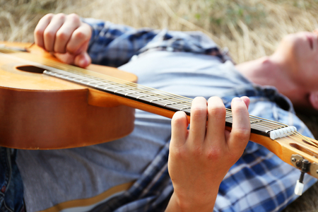 Attractive boy lying on the grass and playing guitar, outdoors