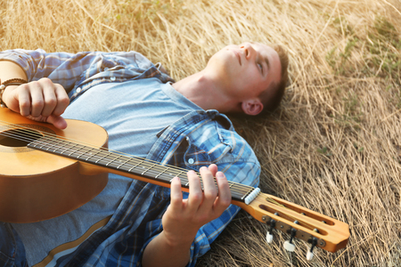 Attractive boy lying on the grass and playing guitar, outdoorsの写真素材