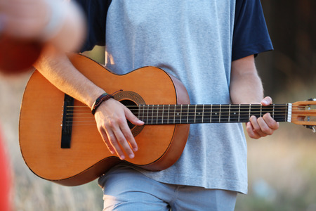 Attractive boy lying on the grass and playing guitar, outdoorsの写真素材