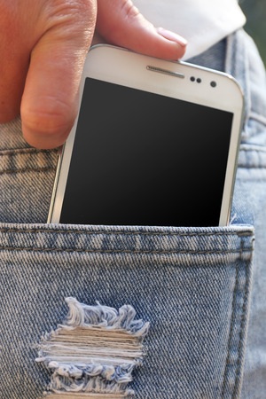 Female hand puts white smart mobile phone into jeans pocketの写真素材