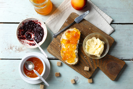 Tasty jam in the jar and bowls, butter, fresh bread and crackers on blue wooden backgroundの写真素材
