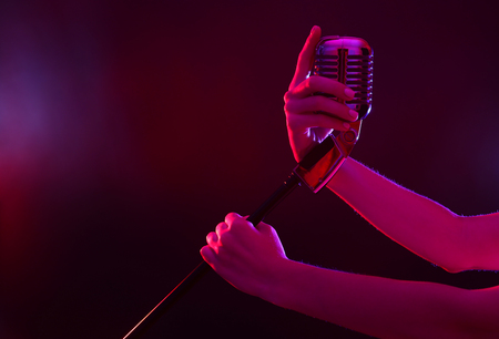 Female hand holding a retro microphone against colourful backgroundの写真素材
