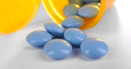 Blue drugs spilled from yellow pill bottle on white background, close up