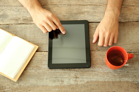 Workplace - tablet, book and red cup of tea on wooden tableの写真素材