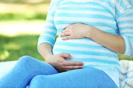 Cute happy pregnant woman on white blanket in the park, close upの写真素材