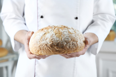 Baker checking freshly baked bread in kitchen of bakeryの写真素材