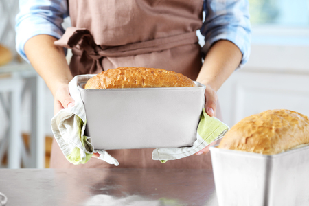 Baker checking freshly baked bread in kitchen of bakeryの写真素材