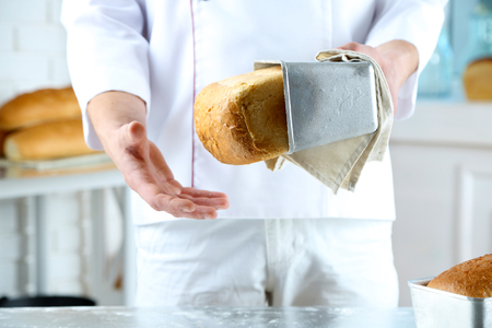 Baker checking freshly baked bread in kitchen of bakeryの写真素材