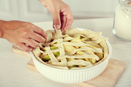 Woman making apple pie on wooden table, on light backgroundの写真素材