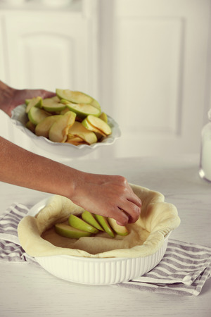 Woman making apple pie on wooden table, on light backgroundの写真素材