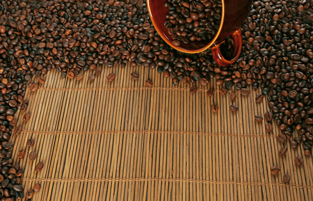 A brown cup and aromatic coffee beans scattered on bamboo matの写真素材