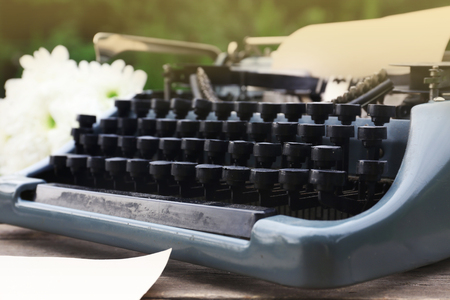 Vintage black typewriter with  old books and flowers on wooden table, outdoorsの写真素材