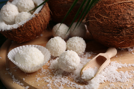 Candies in coconut flakes and fresh coconut on wooden board, close-upの写真素材