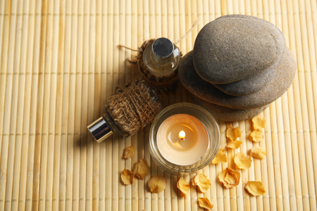 Beautiful composition with candle, aroma oil and pebbles on bamboo matの写真素材