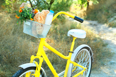 Beautiful yellow bicycle with bouquet of flowers, milk bottle and bread in basket, outdoorsの写真素材