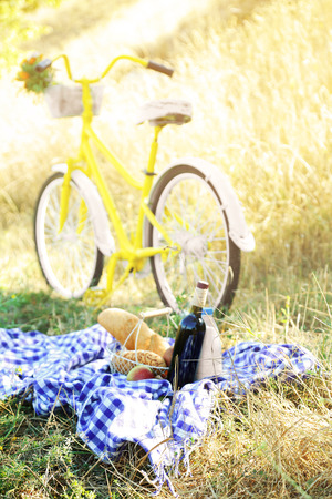 Old yellow bicycle and picnic snack on checkered blanket on grass in parkの写真素材