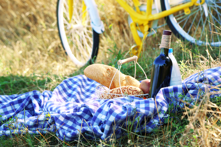 Old yellow bicycle and picnic snack on checkered blanket on grass in parkの写真素材