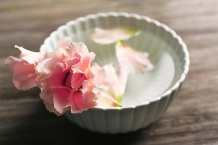Tender pink rose and petals in a bowl of water on wooden background