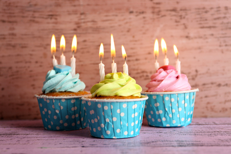 Tasty cupcakes with candles on violet table against wooden backgroundの写真素材