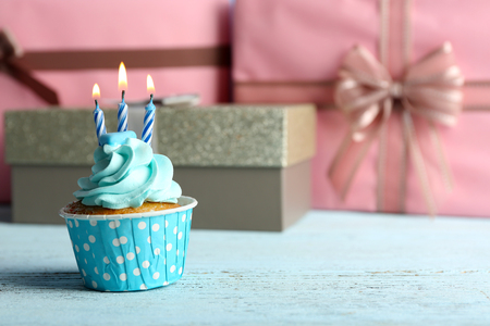 Sweet cupcake with candle on blue wooden table against pink present boxesの写真素材