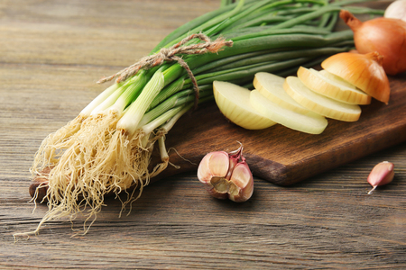 Fresh different onions with garlic on board against wooden backgroundの写真素材