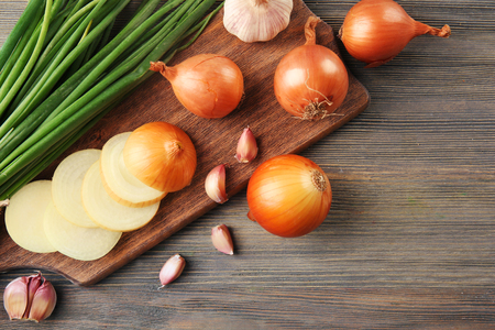 Fresh different onions with garlic on board against wooden backgroundの写真素材