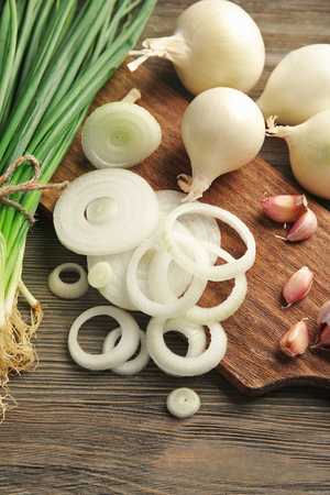 Onions circles, fresh green onion with garlic on board against wooden backgroundの写真素材