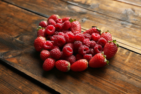 Heart shaped strawberries and raspberries on wooden background