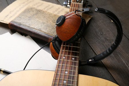 Acoustic guitar, headphones, musical notes and white papers on wooden background, close upの写真素材