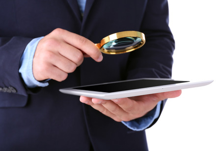 Businessman holding magnifying glass and digital tablet, isolated on white, searching and examining conceptの写真素材