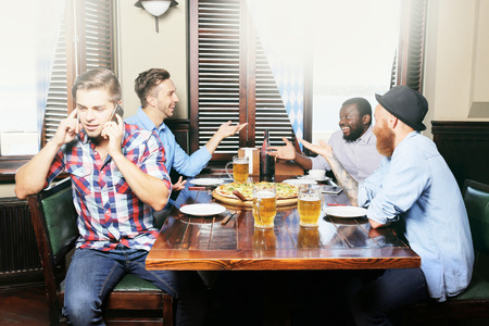 Young men drinking beer and talking in cafeの写真素材